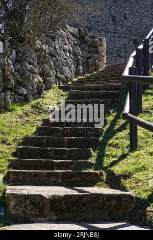 Una scena all'aperto con scale che salgono su un muro di pietra, con erba verde in primo piano. Foto Stock