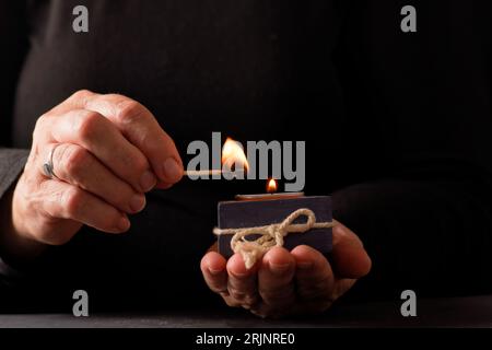 Le mani di una donna che accende una candela con uno sfondo nero e uno spazio per le copie Foto Stock