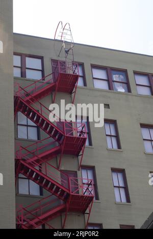 Una scala antincendio in ferro rosso conduce ad una finestra al secondo piano contro un muro di mattoni Foto Stock