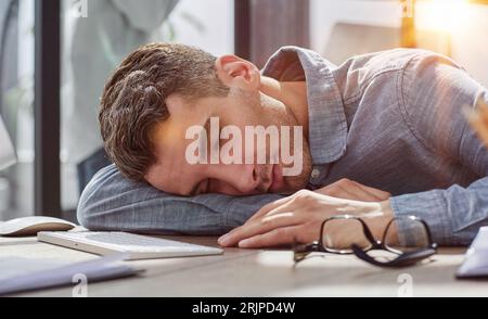 Uomo d'affari stanco che dorme sulla sua scrivania di fronte al computer portatile, lavora troppo, si sente esausto in un ufficio moderno. Foto Stock