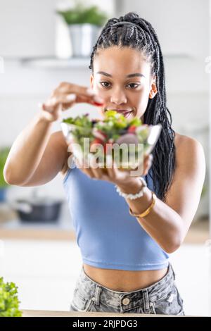 Giovane donna afroamericana prepara insalata sana, aggiunge pomodori. Foto Stock