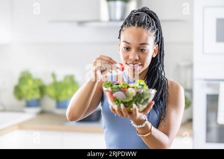 Giovane donna afroamericana prepara insalata sana, aggiunge pomodori. Foto Stock