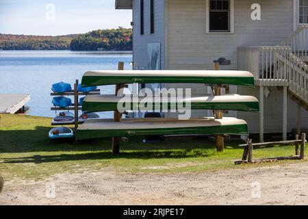 Una collezione di canoe con kayak sullo sfondo arroccate su una cremagliera accanto a un lago. Foto Stock