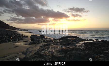 Una splendida vista del sole che tramonta sull'oceano da un'area spiaggia, con rocce in primo piano Foto Stock