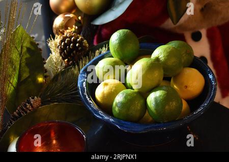 Una ciotola in ceramica blu piena di limone e limoni si trova su un tavolo di legno accanto a ornamenti decorativi Foto Stock