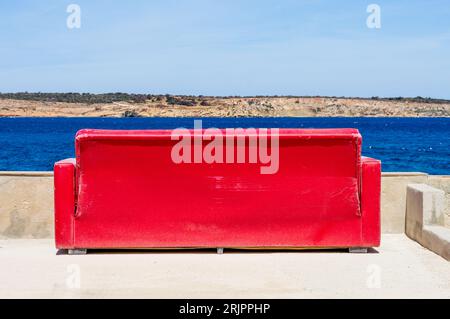 Divano rosso sulla riva del Mar Mediterraneo, Mellieħa, Malta Foto Stock