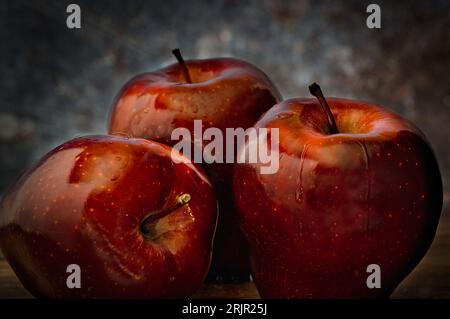 Un primo piano di mele rosse biologiche sedute su un rustico tavolo di legno, con uno sfondo sfocato Foto Stock
