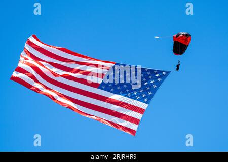 La bandiera americana che si getta nel vento, attaccata a un paracadute colorato sospeso in aria Foto Stock