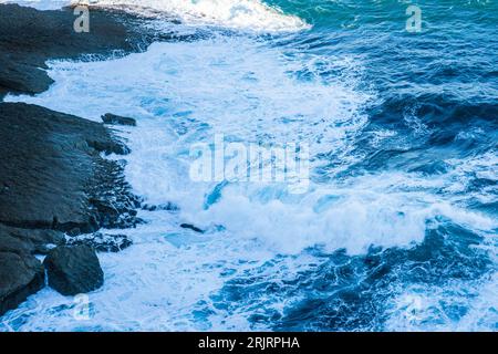 Un'immagine ad alto angolo di onde schiumose che si schizzano contro una costa rocciosa Foto Stock