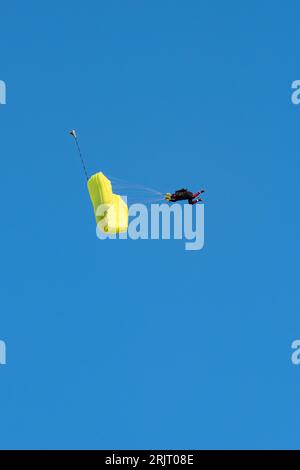 Vista mozzafiato di un paracadutista con un paracadute giallo e un cielo blu sullo sfondo Foto Stock