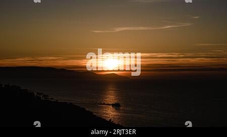 Un maestoso tramonto arancione illumina l'orizzonte sull'oceano lontano. Foto Stock