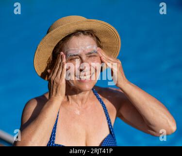 Ritratto di una donna anziana che applica la crema solare al viso mentre è in vacanza. Foto Stock