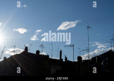 Una vista delle antenne TV in piedi sulla silhouette dei tetti contro un cielo blu Foto Stock