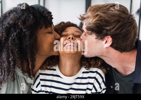 Figlia felice seduta tra genitori che la baciano sulle guance Foto Stock