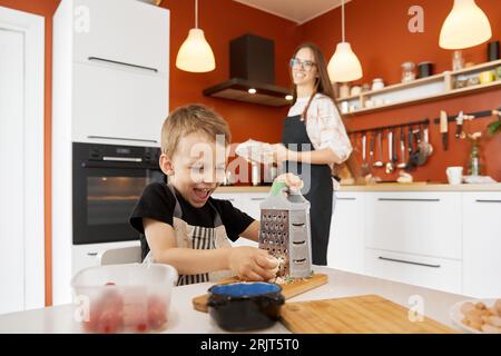 Happy boy grattugia il formaggio e prepara il cibo con la madre a casa Foto Stock