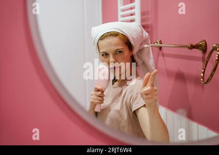 Giovane donna giocosa che si muove nello specchio del bagno Foto Stock