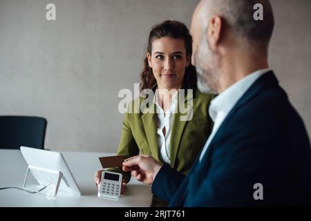 Donna d'affari sorridente con un uomo d'affari che paga con carta di credito Foto Stock