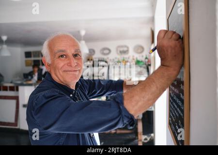 Sorridente proprietario di un caffè che scrive a bordo con la penna Foto Stock