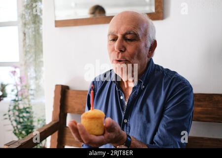 Un uomo anziano che soffia una candela sul cupcake Foto Stock