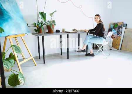 Artista seduto sulla sedia e che lavora in officina Foto Stock
