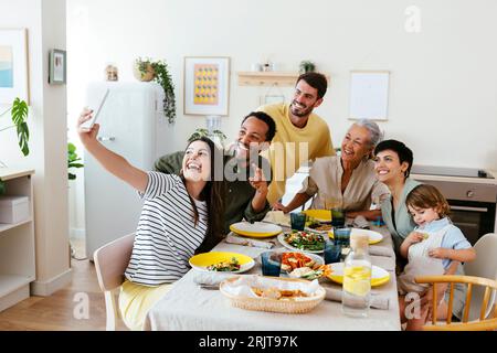 Famiglia sorridente che scatta selfie seduti al tavolo da pranzo in cucina Foto Stock
