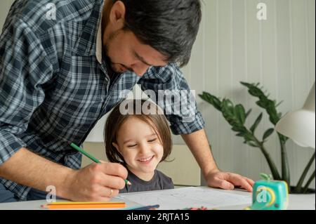 Padre che assiste il figlio a disegnare con matite colorate a casa Foto Stock