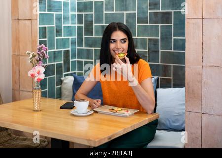 Giovane donna che si gusta degli spuntini con il caffè nella caffetteria Foto Stock
