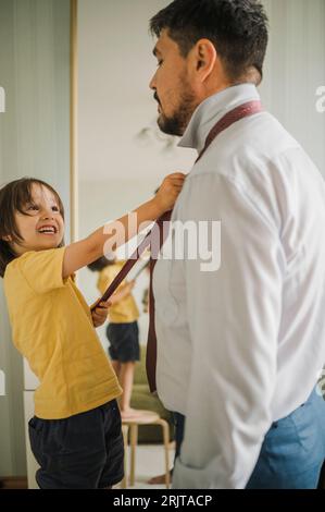 Figlio sorridente che regola la cravatta del padre a casa Foto Stock