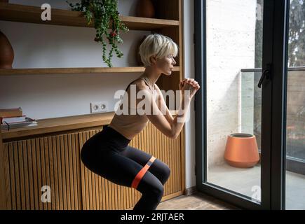 Donna bionda che fa esercizi di squattamento a casa Foto Stock