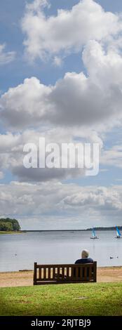 Un uomo solitario siede su una panchina in riva al lago. Foto Stock