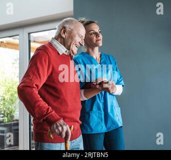 Infermiera sorridente che si prende cura e si tiene per mano con un anziano a casa Foto Stock