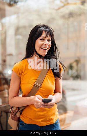 Donna matura allegra in piedi con lo smartphone Foto Stock
