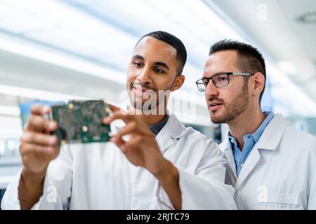 Due colleghi che discutono sulla scheda madre in una fabbrica di elettronica Foto Stock