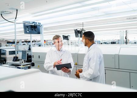 Team di tecnici elettrici competenti in camici da laboratorio che si riuniscono in una fabbrica di elettronica Foto Stock