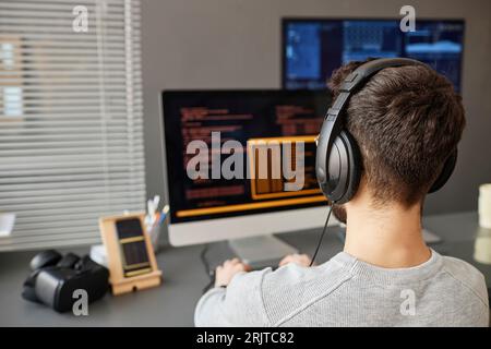 Giovane programmatore di computer che indossa cuffie che lavorano su PC desktop Foto Stock