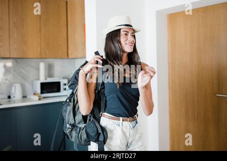 Giovane donna felice in piedi con lo zaino nell'appartamento Foto Stock