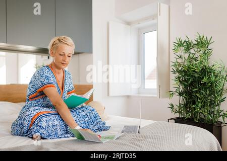 Donna matura che legge una cartina sul letto in camera da letto Foto Stock