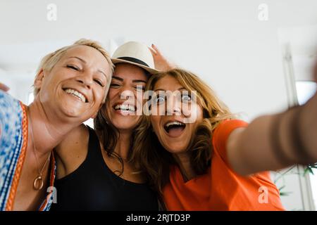 Donna allegra che fa selfie con gli amici in appartamento Foto Stock