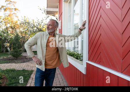 Uomo contemplativo che si appoggia vicino alla finestra della casa Foto Stock