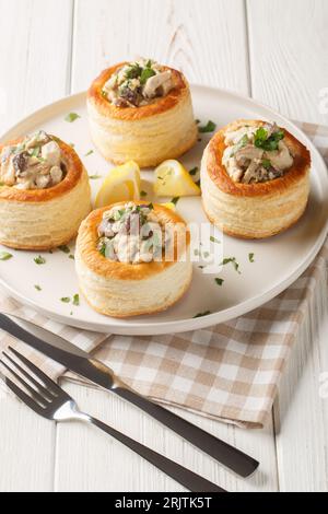 Pasta sfoglia francese Vol au vent ripieno con pollo, panna e primi piani di funghi sul piatto sul tavolo di legno bianco. Verticale Foto Stock