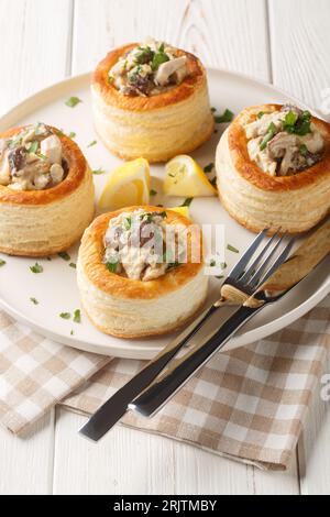 Gustosa pasta sfoglia vol-au-vent ripiena di pollo, funghi e crema per primo piano sul piatto sul tavolo di legno bianco. Verticale Foto Stock