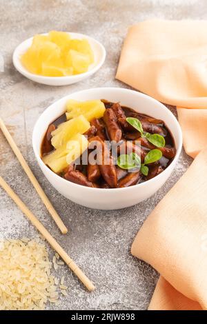 Tteokbokki o Topokki, bastone di torta di riso fritto, popolare Street food coreano con salsa jjjajang piccante e ananas su sfondo grigio cemento e arancio Foto Stock