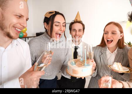 Gruppo di giovani amici con champagne per festeggiare il compleanno in ufficio Foto Stock