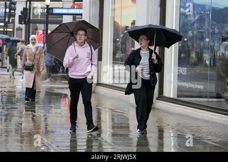 Le persone si rifugiano sotto gli ombrelloni durante il tempo umido nel centro di Londra. Foto Stock