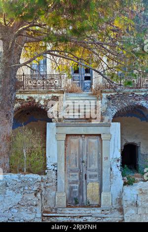 Bella villa vecchia e abbandonata, con una tradizionale porta d'ingresso in legno e scale che conducono all'edificio principale e un grande pino. Foto Stock