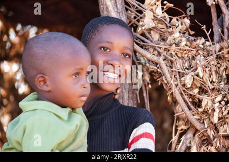 Bambini africani nel villaggio, sorella che tiene suo fratello davanti a una capanna Foto Stock