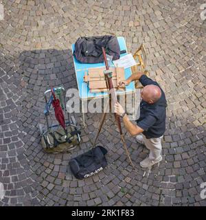 Pittore di strada dipinge quadri per i turisti durante i suoi preparativi nel centro storico di Malcesine in Italia Foto Stock