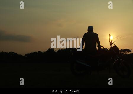 Young man sitting on a bike and enjoying the sunset Foto Stock