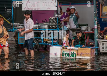 Il padre tailandese tira i suoi figli attraverso le acque alluvionali su una zattera improvvisata. Phahon Yothin Road, Bangkok, Thailandia. © Kraig Lieb Foto Stock