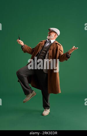 Foto a tutta lunghezza. Uomo maturo ed emotivo con baffi, vestito in stile vintage, sembra un detective, ridendo mentre balla. Foto Stock